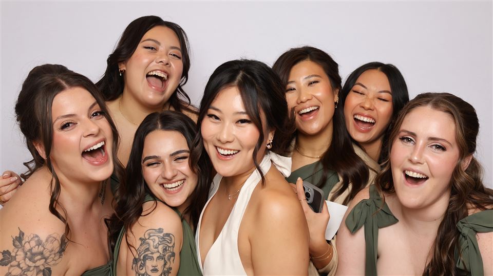 Seven wedding guests laugh together in an open-air photo booth portrait