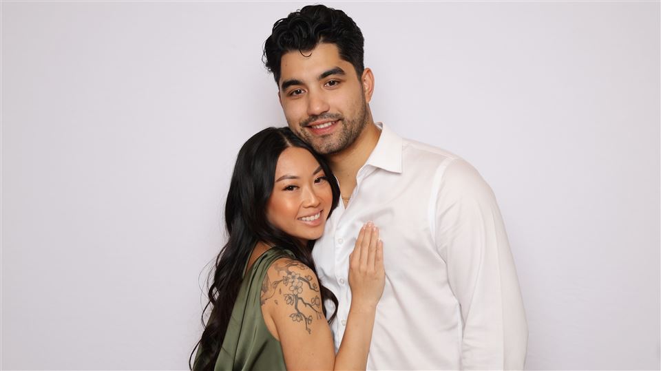 A couple poses together against a white photo booth backdrop