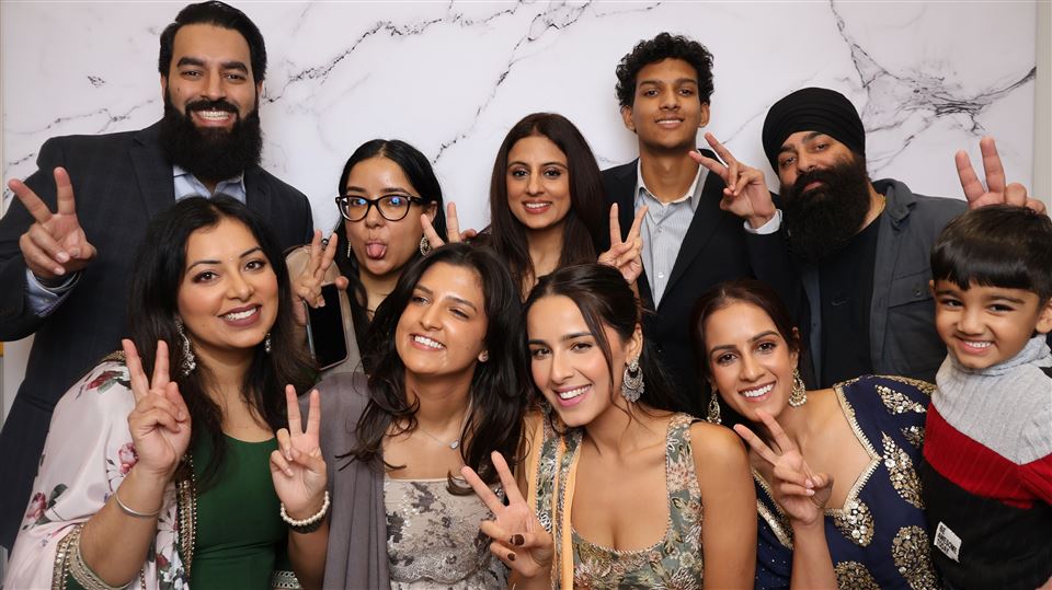 A large group of wedding guests make peace signs in front of a marble photo booth backdrop