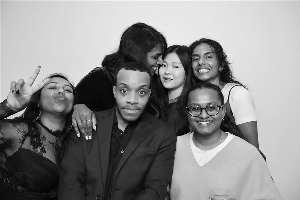 Six event guests pose together in a black-and-white photo booth portrait