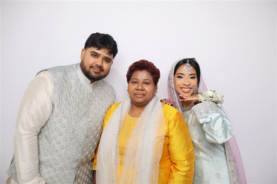 Three wedding guests in formalwear pose together against a white photo booth backdrop