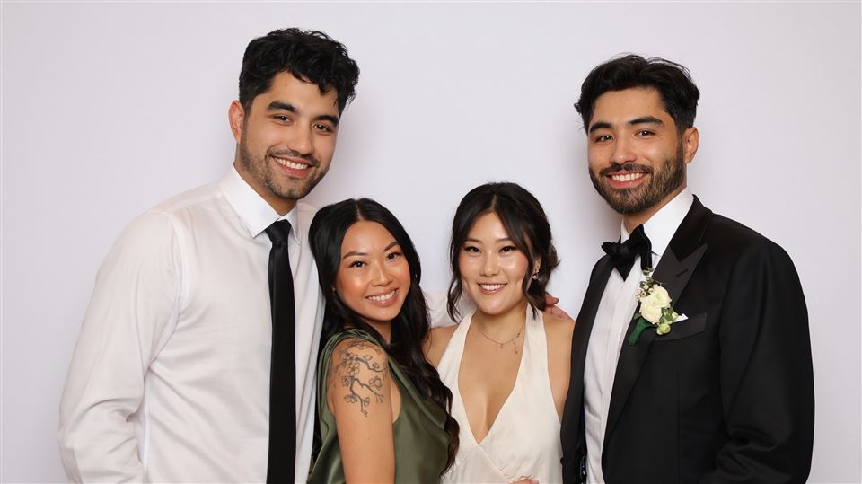 Four wedding guests in formal attire pose together for an open-air photo booth portrait